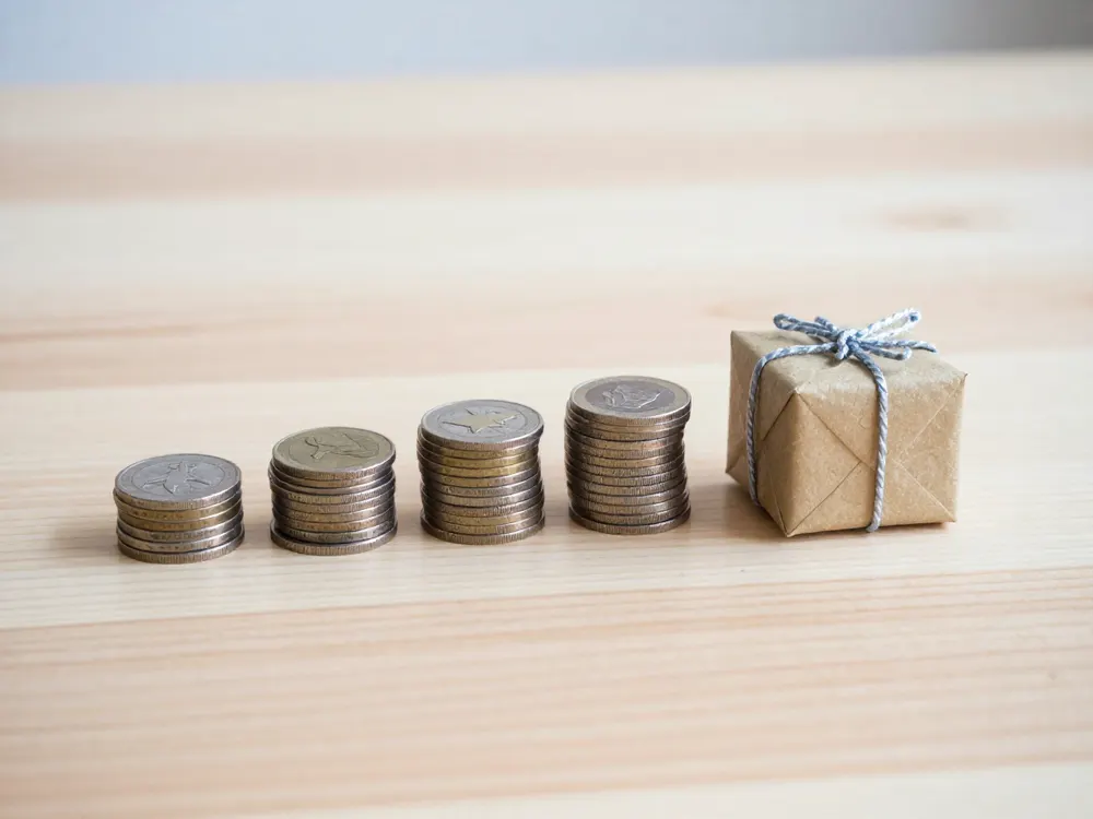 Four stacks of coins in a row beside a small kraft-wrapped gift box, like a price split into four payments