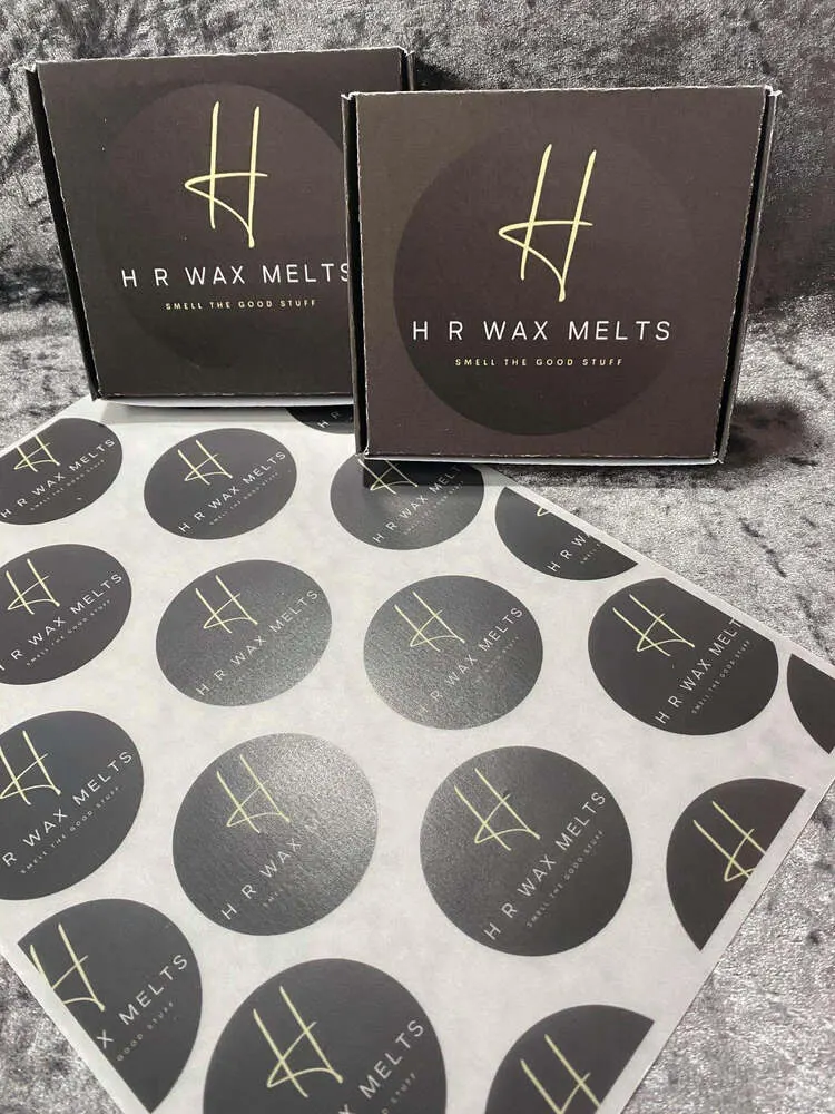 Black logo-printed wax melt boxes resting on a sheet of round logo prints