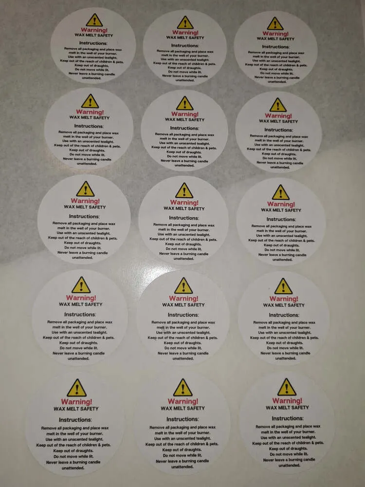 Printed wax melt safety stickers in rows, each with a warning triangle and burning advice